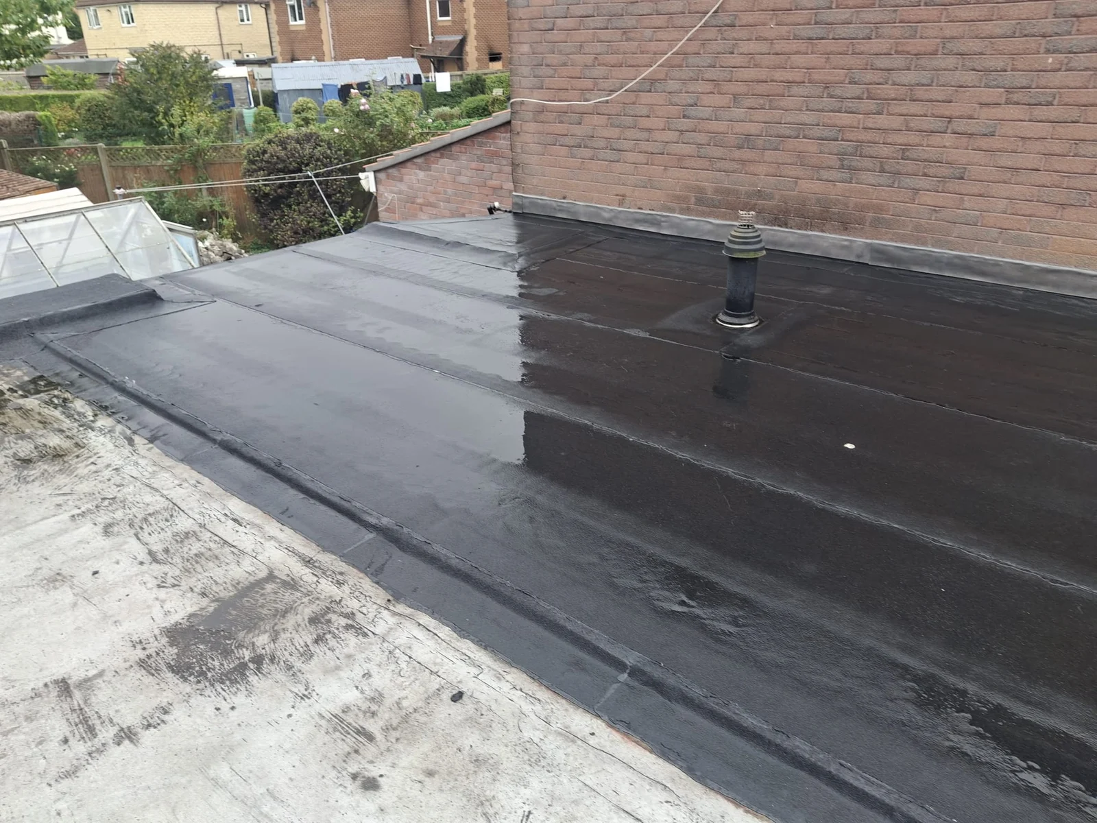 Flat-roof covering alongside a brick wall